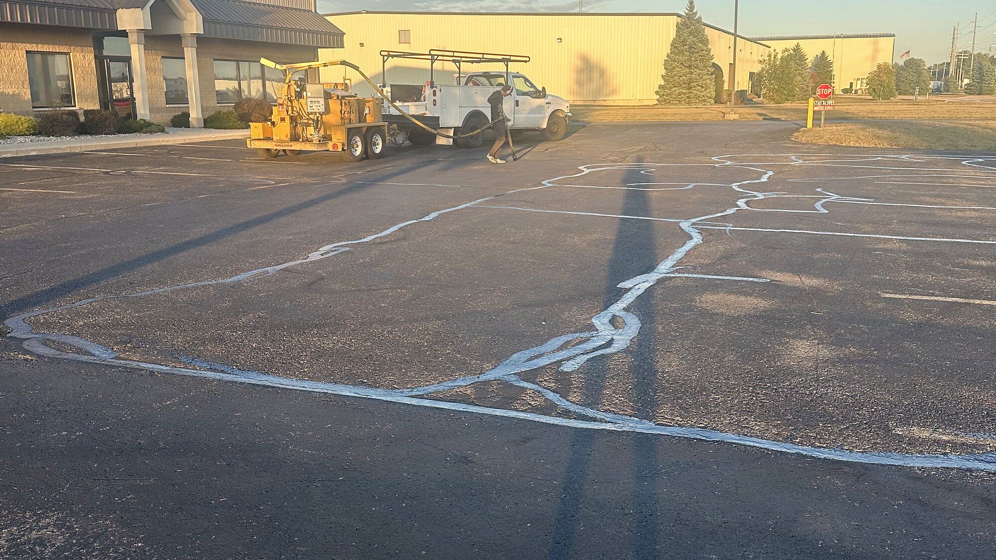 Summer Sealers crew with hot rubber crack filling machine and truck working on a commercial parking lot at golden hour