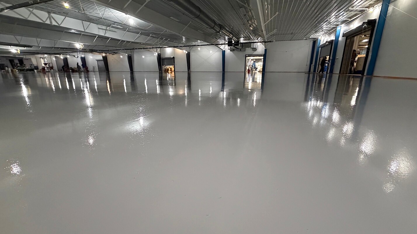 High-gloss gray epoxy floor in a large industrial warehouse with reflective surface and overhead lighting